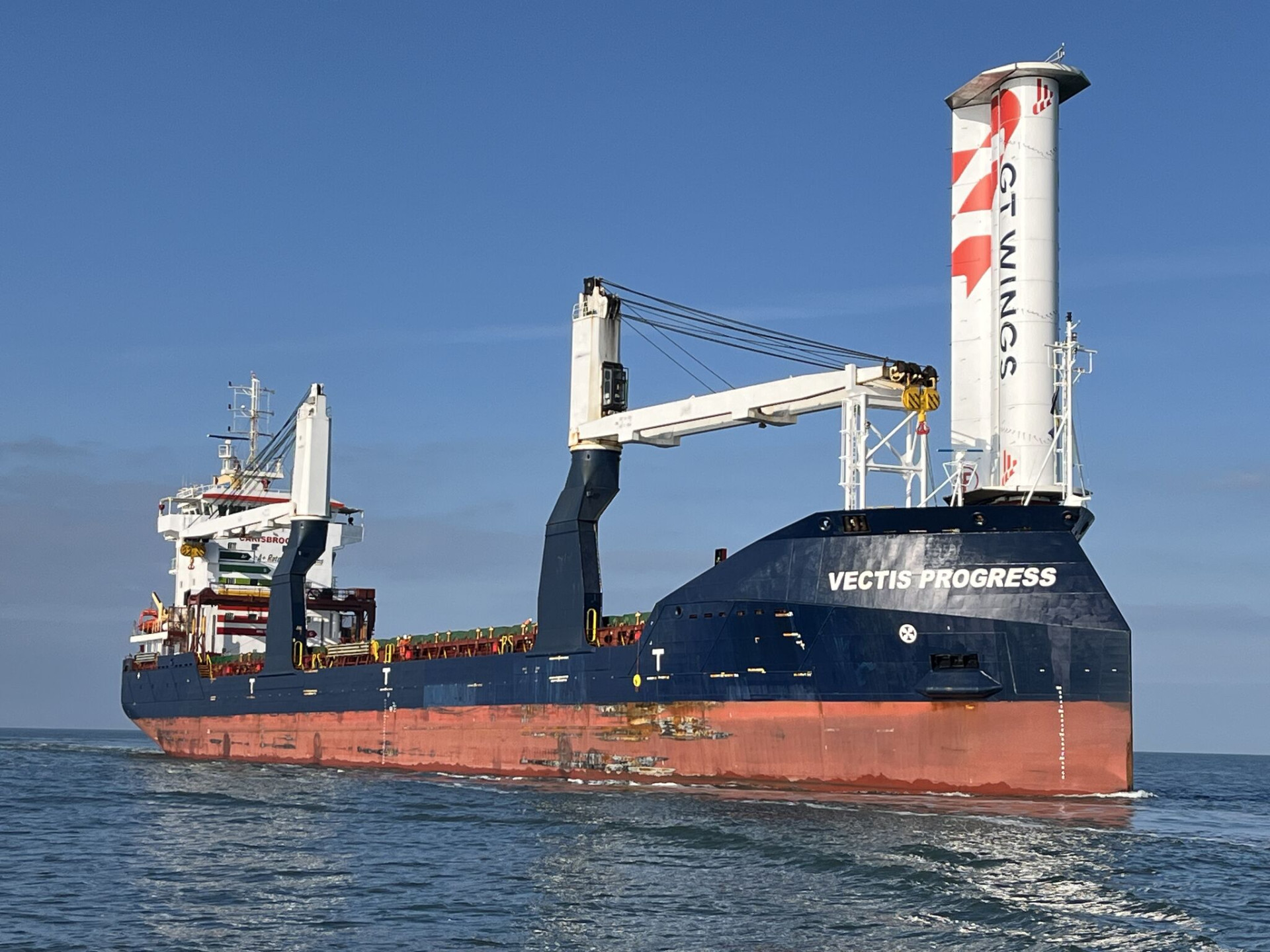 Cargo ship at sea with a single vertical wind rotor for wind-assisted propulsion